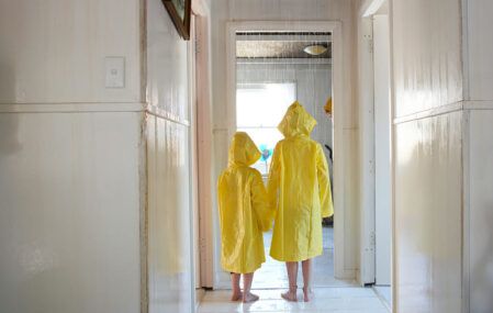 two children stand inside rainy house