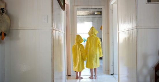 two children stand inside rainy house