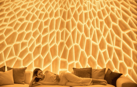 A woman lying down in front of San Vicente's 3D-Printed Light Wall.