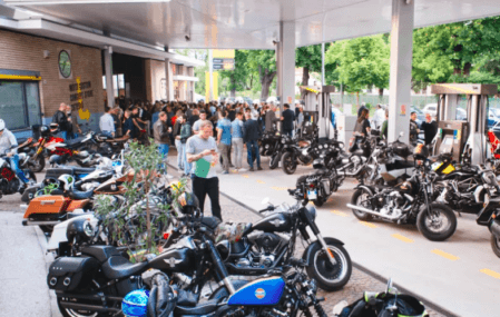 A horde of motorcycles parked outside the new Filling Station Motel, with a group of people mingling in the background.