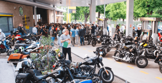 A horde of motorcycles parked outside the new Filling Station Motel, with a group of people mingling in the background.