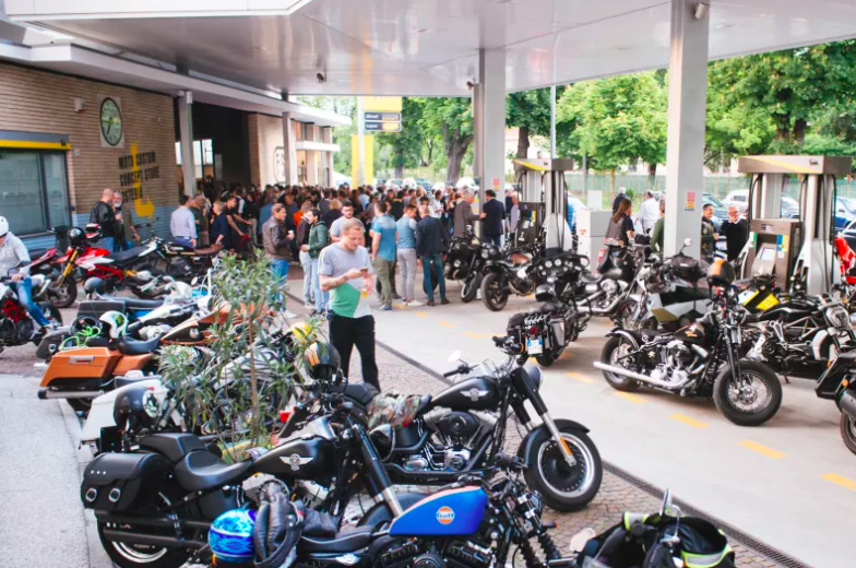 A horde of motorcycles parked outside the new Filling Station Motel, with a group of people mingling in the background. 