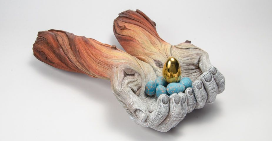 A ceramic sculpture by Christopher David White, this one depicting a pair of outstretched arms holding a few small blue and gold eggs.