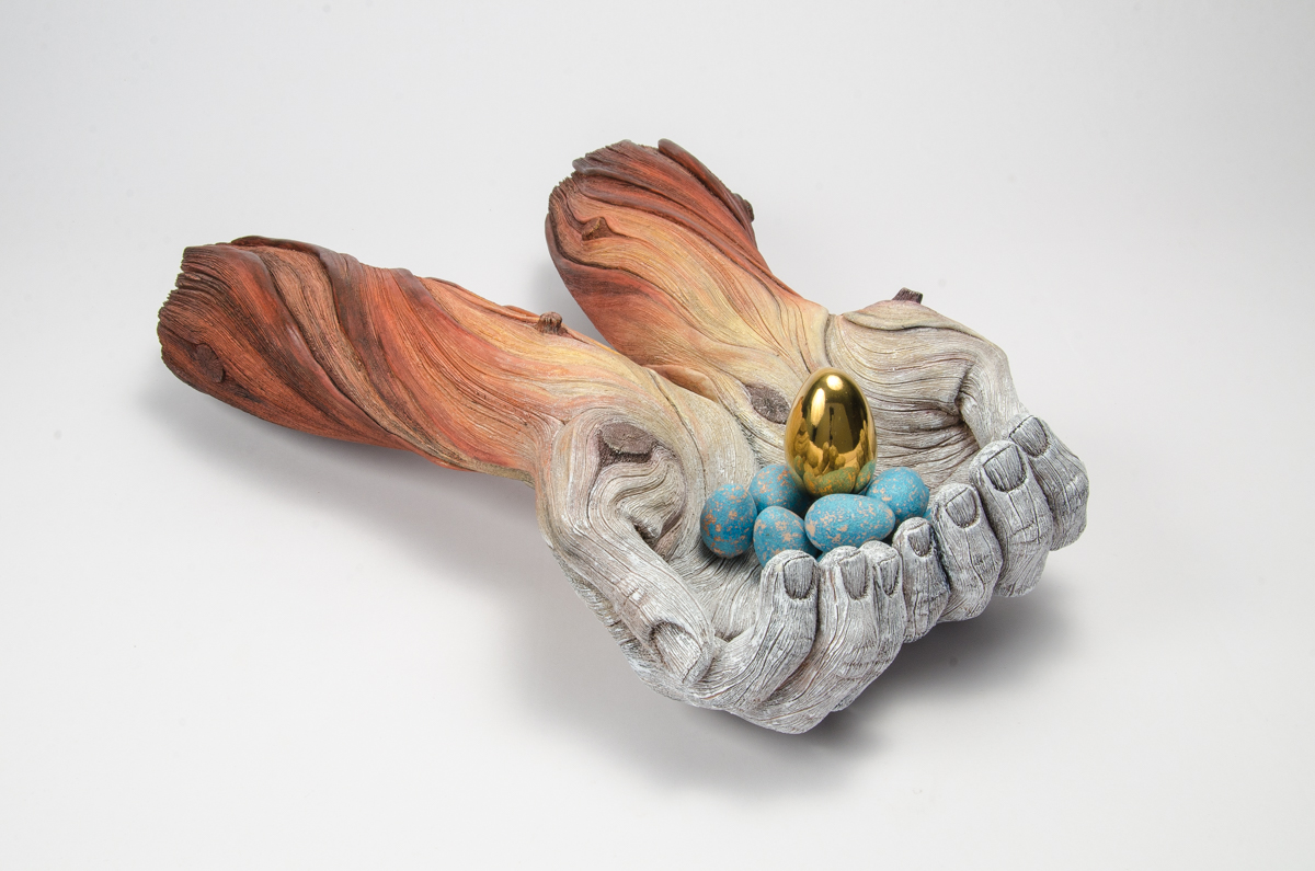 A ceramic sculpture by Christopher David White, this one depicting a pair of outstretched arms holding a few small blue and gold eggs. 