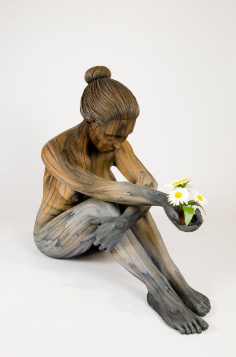 A ceramic sculpture by Christopher David White, this one depicting a sad-looking seated woman holding flowers in her outstretched hands.