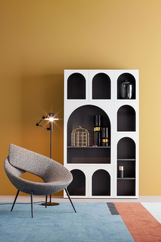 Fabrice Berrux' new Cabinet de Curiosité set against a mustard wall, with a modern chair and lamp off to the side.
