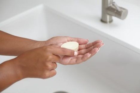 Someone holding a sustainable shampoo bar over a bathroom sink.