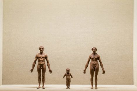 Three clay statues standing next to each other: one of a man (left), one of a child, and one of a woman (right).