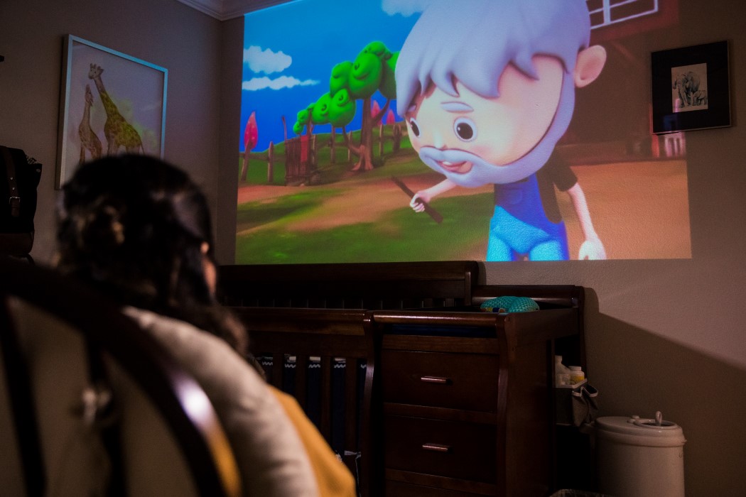 Woman enjoys a cartoon being projected onto her wall from the PIQO tiny projector. 