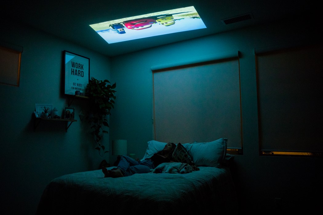 Woman lays in bed as her PIQO tiny projector displays content on her ceiling. 