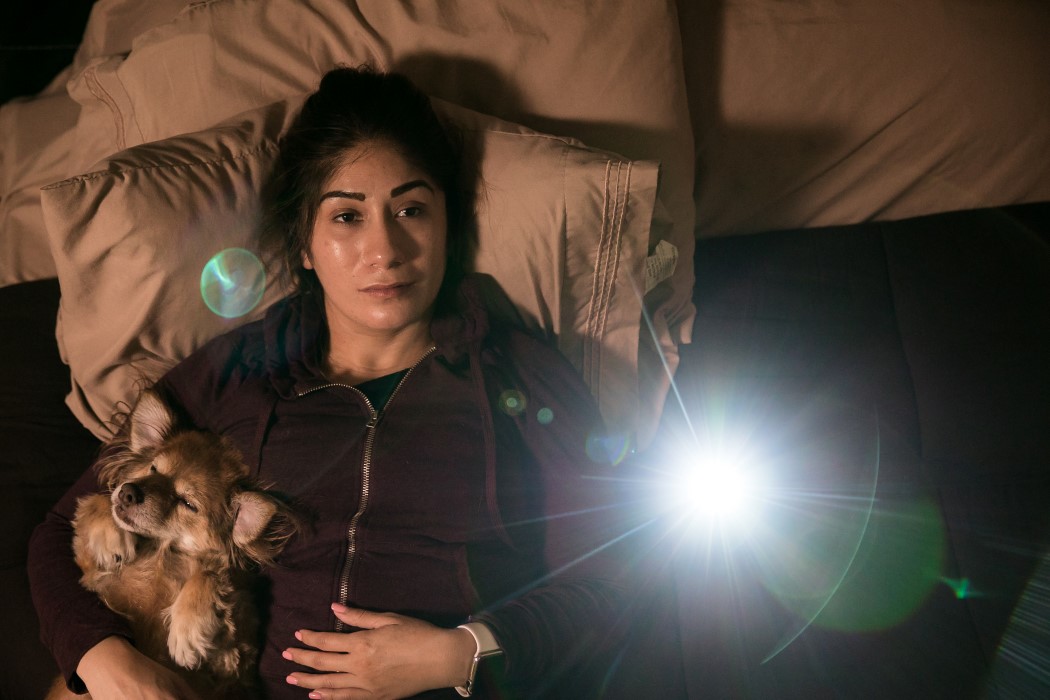 Woman lays in bed as her PIQO tiny projector displays content on her ceiling. 