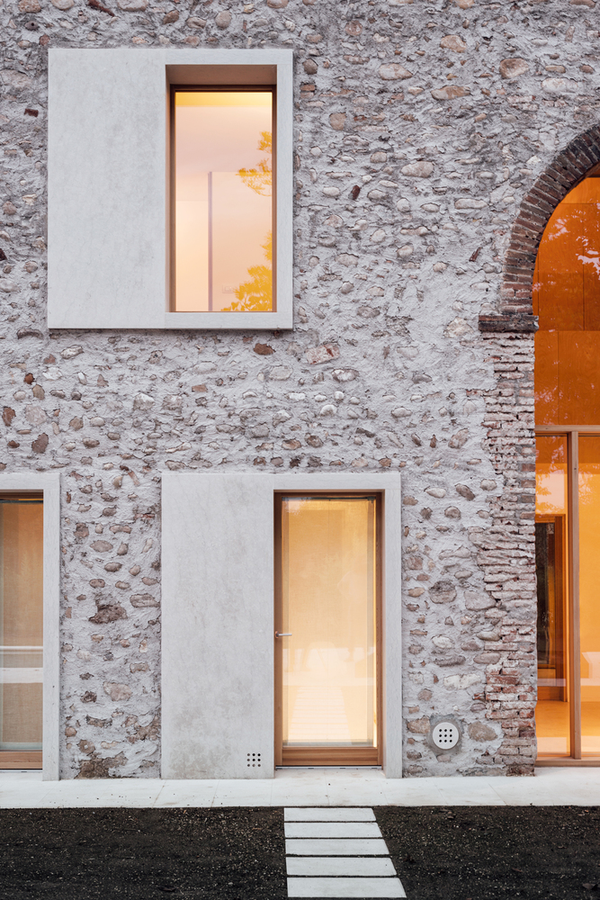 A close-up of the front facade of "A Country Home in Chievo," with all the lights on inside.