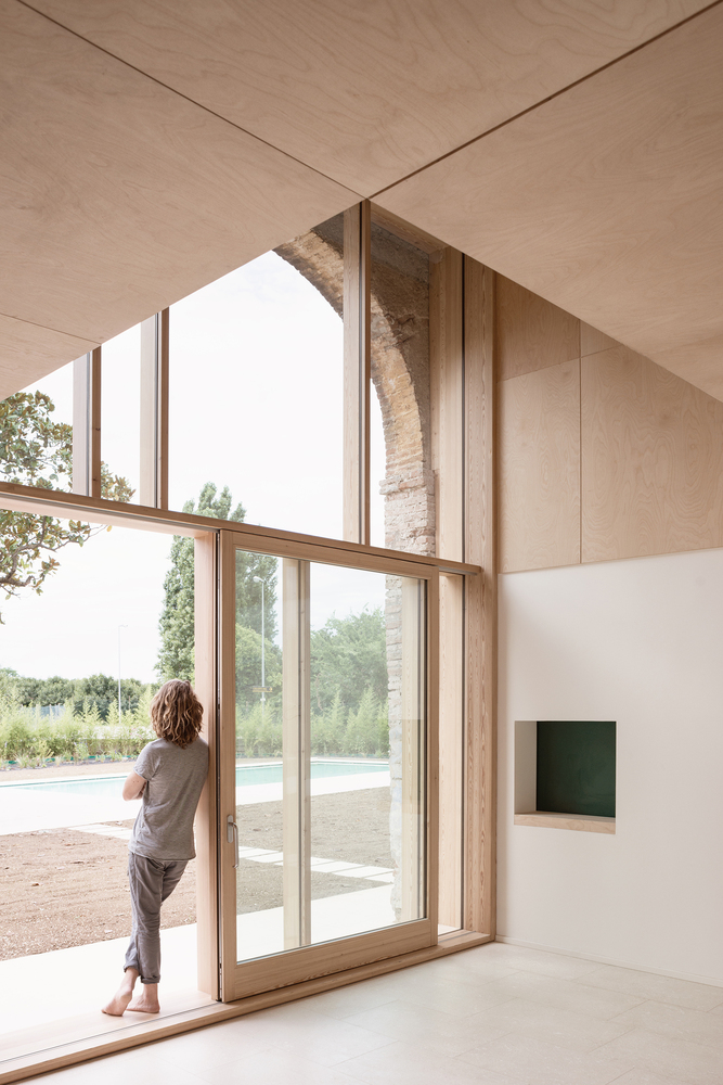 A person leans on the wooden frame of A Country Home in Chievo's operable glazing, gazing out at the garden beyond.