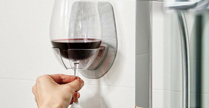 The Sipski Wine Glass Holder mounted to a shower wall, with a glass of red wine nestled firmly inside it.