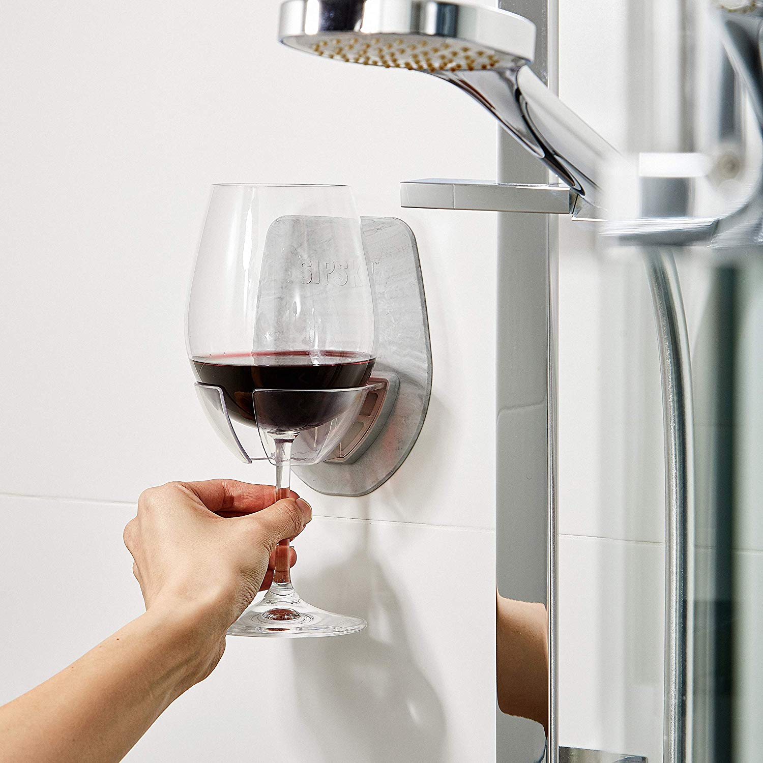 The Sipski Wine Glass Holder mounted to a shower wall, with a glass of red wine nestled firmly inside it. 