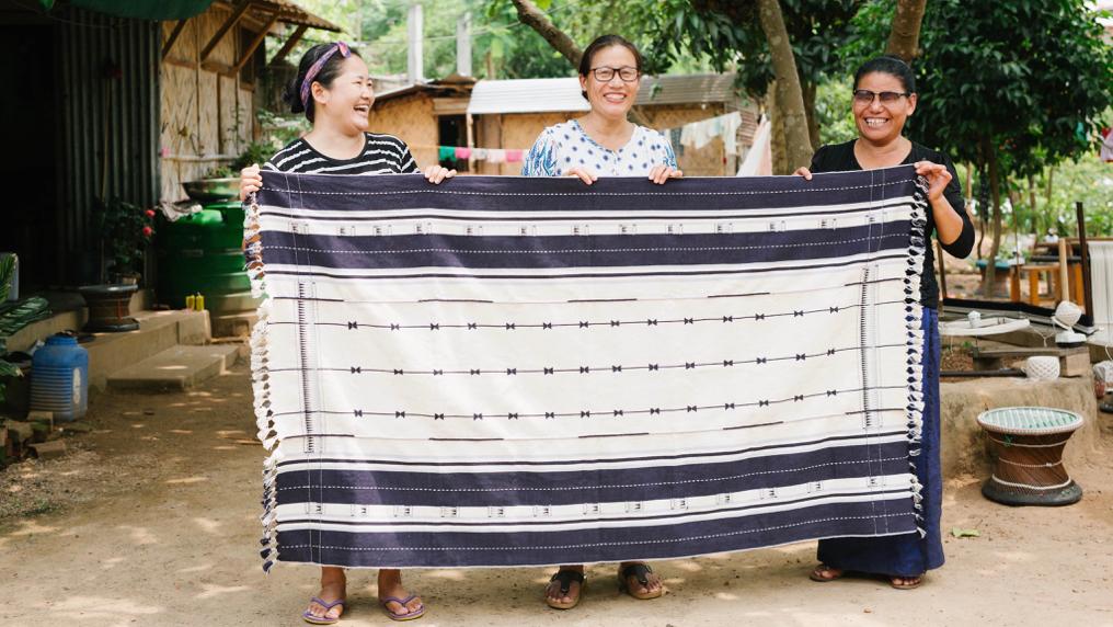 Three artisan textile makers from India's Nagaland region hold up one of their decorative throws.