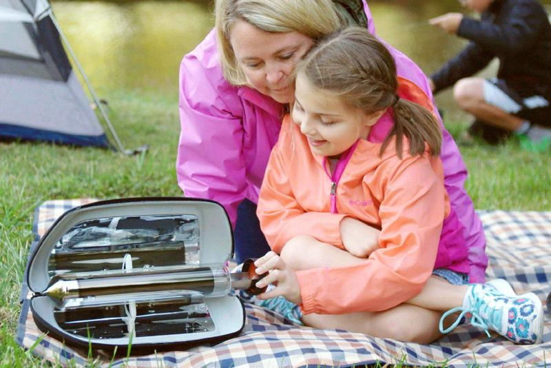 A woman and her daughter cook outside with their GoSun Go Portable Solar Cooker.