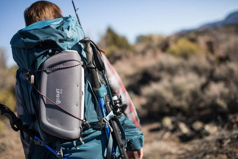 Man hikes up a mountain with a GoSun Go Portable Solar Cooker strapped to his backpack.