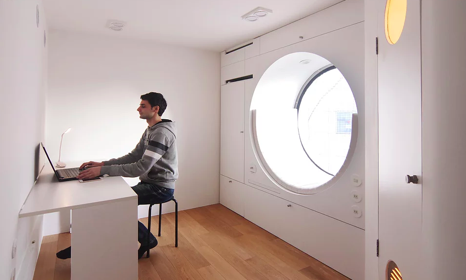 Man works in his renovated micro apartment, complete with a built-in Capsule custom window seat. 