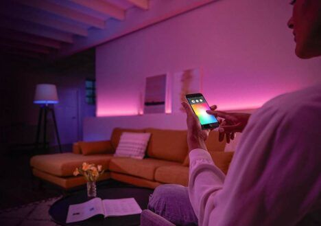 A young woman uses her smartphone to change the color of her smart lights.
