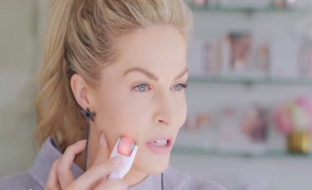 A woman uses the BeautyBio GloPRO Microneedling Facial Regeneration Tool on her face. 