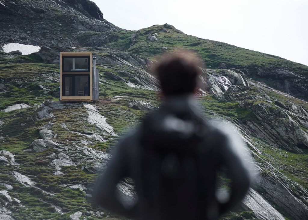 Hiker approaches the mirrored On Mountain Hut, located in the Swiss Alps on the Piz Lunghin