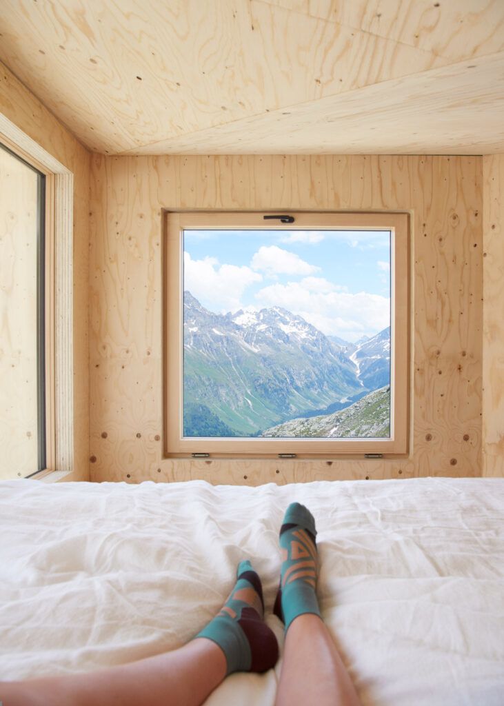 A weary hiker takes in the views from the lofted bed inside the On Mountain Hut