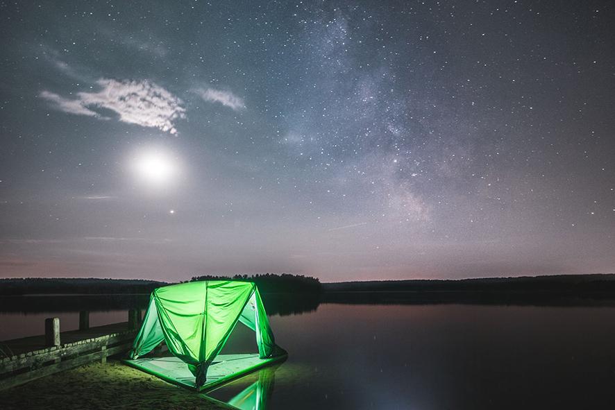 The Universe 5-Person Tree Tent floats on a lake and glows a bright green in the twilight.