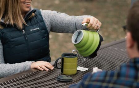 A woman pours hot water from her Voyager kettle while out camping
