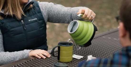 A woman pours hot water from her Voyager kettle while out camping