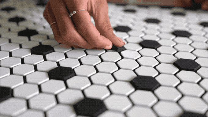 Hand moves the black tiles around to complete a Tile Mat message