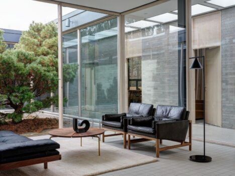 a glass and brick room with stylish furniture next to a courtyard with an evergreen tree
